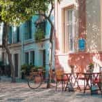 A colorful street in Spain with tables outside in sunlight and trees.