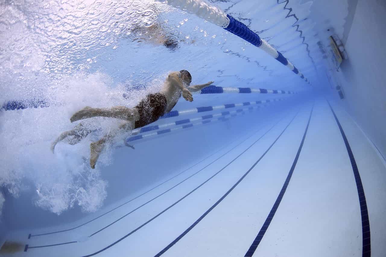 A swimmer doing the front crawl movement underwater while swimming in his lane in an Olympic-sized swimming pool, with another swimmer in the lane to his left.