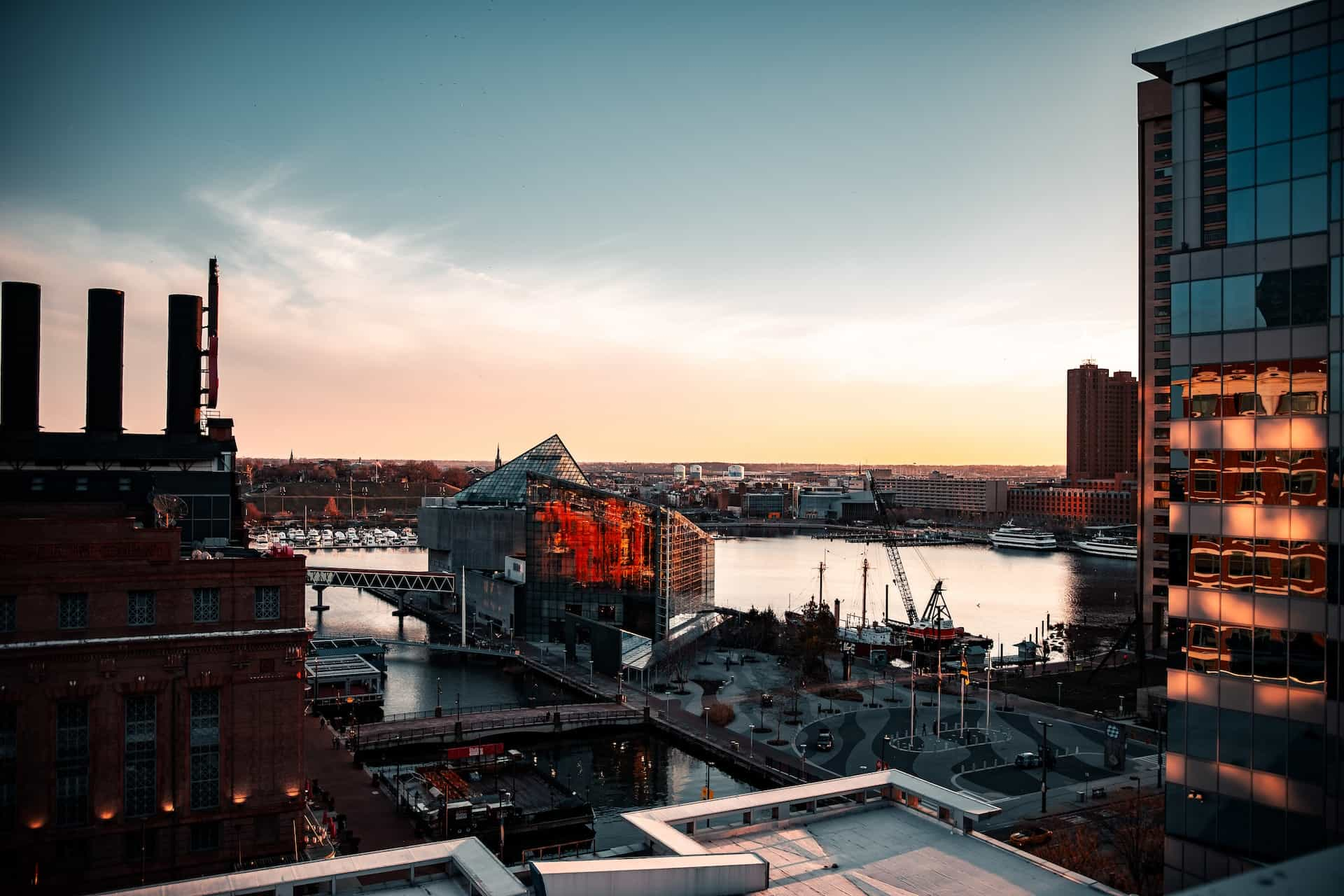 The inner harbor area of downtown Baltimore, Maryland, featuring several skyscrapers and modern building developments along with boats and shipping cranes.