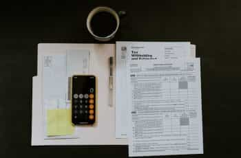 A worktop from above with various tax paperwork, a calculator and a cup of coffee.