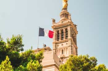 A flag hoisted on a church with a statue on it.